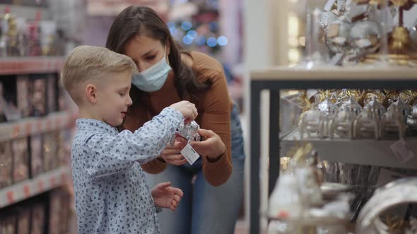 A Mother in a Medical Mask with Her Son at the Mall Choose Home Decorations for Christmas
