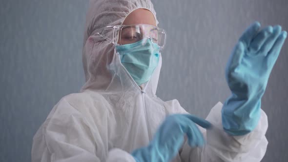 Medic in a Protective Suit Puts on Gloves.