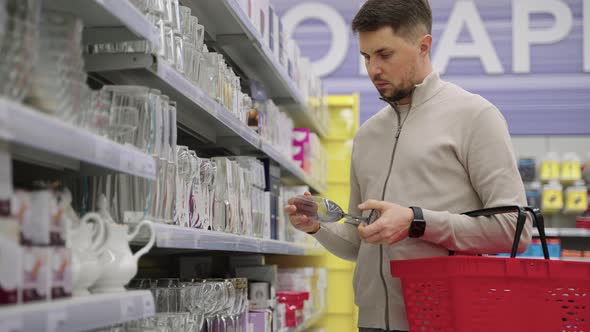 Man is Shopping Alone Choosing Glass for Wine in Supermarket