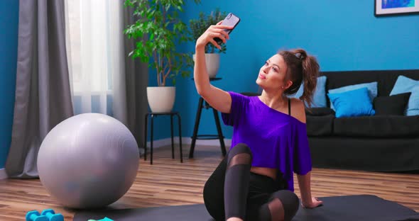 Beautiful Young Woman Dressed in Fitness Clothes Sits on the Wooden Floor of an Apartment