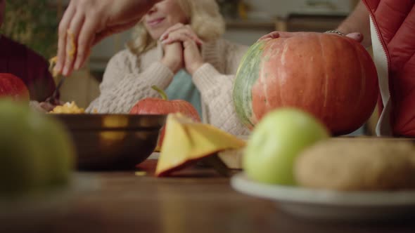 A Man Carves a Pumpkin on the Dinner Table with His Family