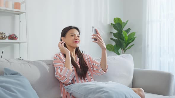 Asian beautiful woman sit on sofa and chat on mobile phone in house.