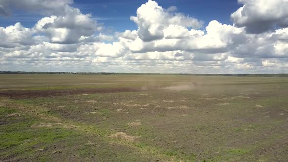 Aerial Green Spring Field and Distant Tractor Raises Dust