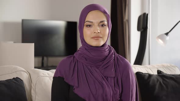 A Young Beautiful Muslim Woman Applauds to the Camera with a Smile As She Sits on a Sofa