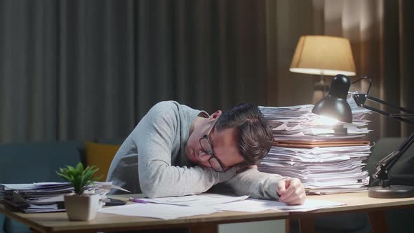 Tired Asian Man Yawning And Sleeping While Working Hard With Documents At Home