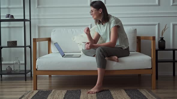Young Woman Using Laptop Relaxing and Watching Video While Sitting on Sofa at Home