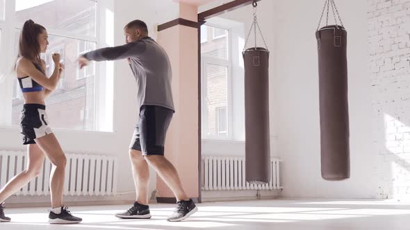 An Experienced Trainer Puts the Technique of Blows To a Young Girl in the Boxing Hall