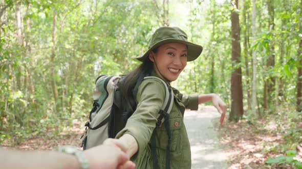 Asian female backpacker hold boyfriend's hand while travel in forest.