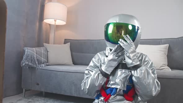 Man in an Astronaut Suit Sits on the Floor in Living Room Next to a Cardboard Model of a Space