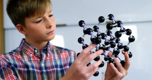 Schoolboy experimenting molecule model in laboratory at school