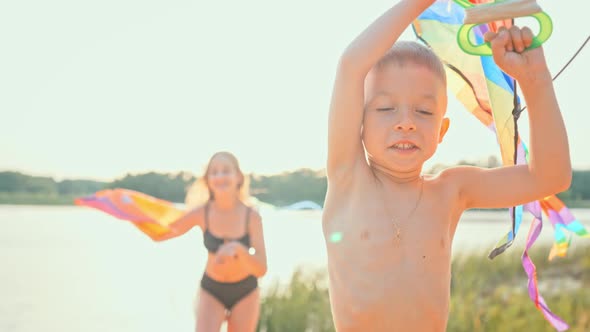 Two Children Running Along Beach in Summer with Kite Flying in Wind