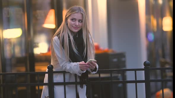 Portrait of Happy Girl Using Mobile Phone on the Evening Cafe Terrace