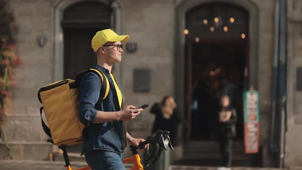 A Young Happy Delivery Man is Going and Holding a Smartphone