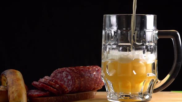 Pouring beer into the glass. Sausage with mug cold craft beer in a glass with water drops