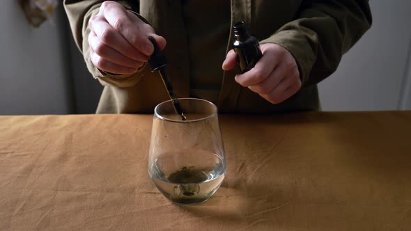 woman adds drops of chlorophyll to glass of water on a table