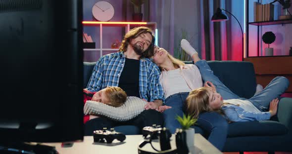 Family Sleeping on the Couch in front of Working TV Set in the Evening