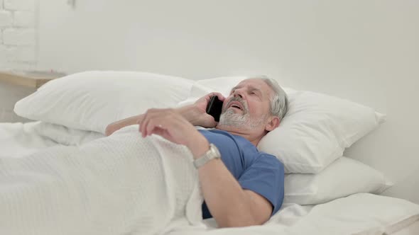 Old Man Talking on Phone Lying in Bed