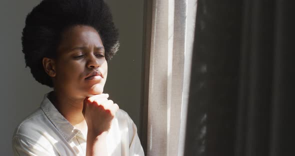 Thoughtful african american woman looking through window in bedroom