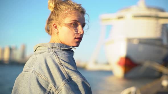 Back View of Charming Blond Girl with Blue Eyes in Jacket Standing in Docks Near Sea and Boat