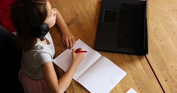 Cute little girl with headphones using laptop to study at home