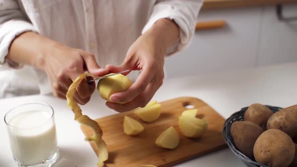 Peeling Potatoes On A White Table. A Woman Peels Raw Potatoes At The Table In The Kitchen, Close Up