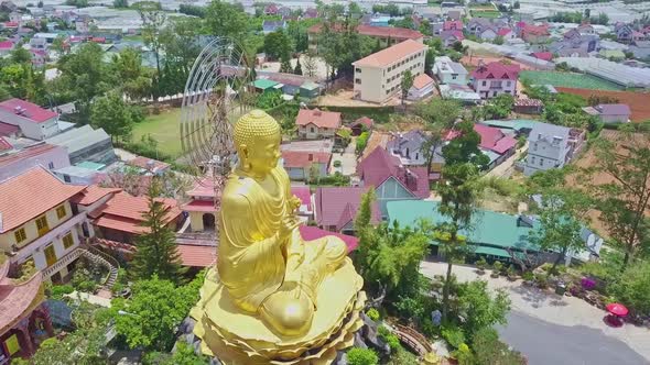 Drone Rotates Above Large Buddha Monument Against Cityscape