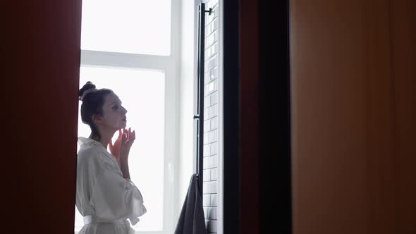 Woman in the Bathroom in Front of the Mirror Puts on a Rejuvenating Face Mask From Wrinkles