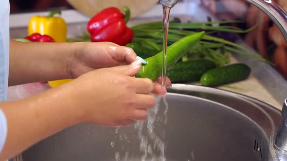 Close-up of Young Girl Washing Chili Peppers in the Sink at Home in the Kitchen