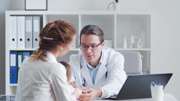 Male pediatrician is examining little baby. Doctor, mother and daughter in medical office.