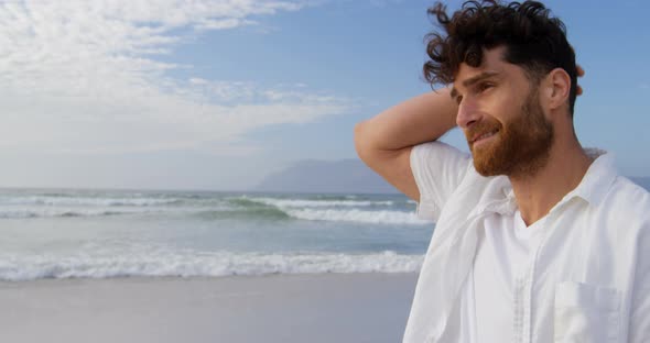 Side view of young caucasian man walking and looking around at beach on a sunny day 4k