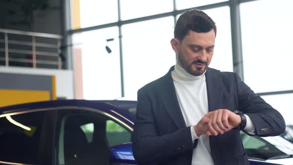 Elegant Man Uses a Smart Watch in Car Showroom