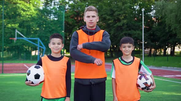 Two Teen Boys in Football Uniforms and their Professional Young Coach Posing on Camera