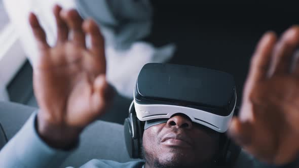 AfricanAmerican Man Wearing Virtual Reality Glasses and Headset Lying on the Sofa