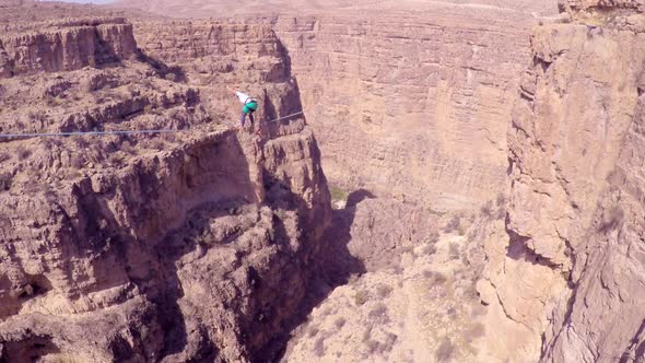 Aerial view of a woman balancing while tightrope walking and slacklining across a canyon