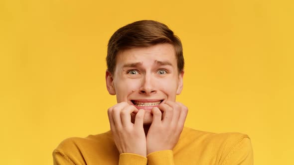 Scared Guy Biting Nails Looking At Camera Over Yellow Background