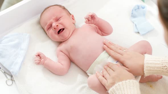 Top View of Young Caring Mother Changing Diapers of Her Newborn Baby Son on Changing Table