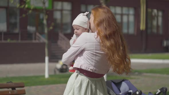 Portrait of Adorable Woman Holding the Baby in Arms and Smiling in the Yard