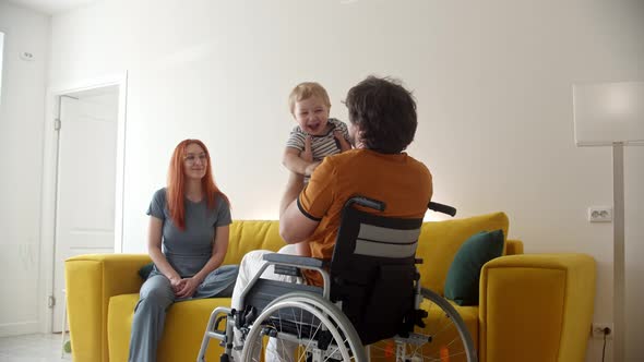 Man in a Wheelchair Playing with His Baby and His Smiling Wife Watching Them