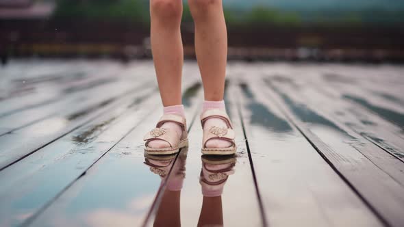 Girl Stamps Feet in Puddle of Rain Water on Wooden Deck