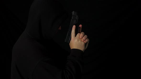 A hooded man with a hand gun pistol in the dark
