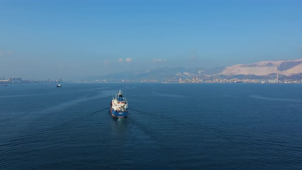 Aerial View Following the Ultra Large Cargo Ship at Sea Leaves Port at Sunny Day