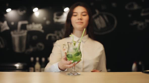 A Beautiful Young Girl Trying a Mojito Cocktail Standing on a Bar Counter