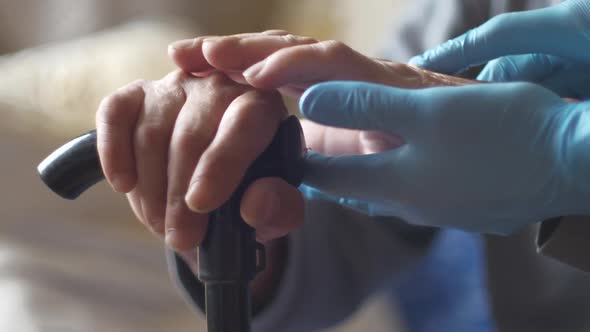 Close-up of the hands of an old man holding a walking stick cane, the hands of a doctor in blue glov