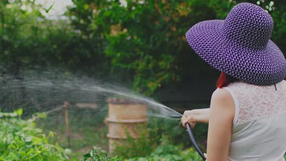 Rear View of Young Woman Watering Vegetable Garden From Hose