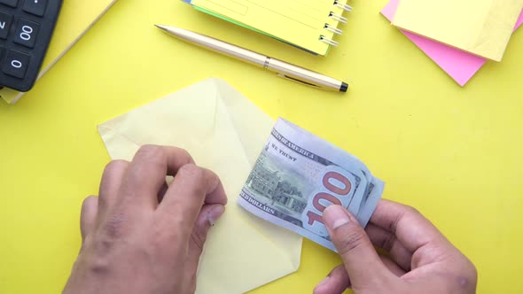 Person Hand Putting Cash in a Envelope on Yellow Background