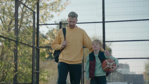 Father with Son Walk Talking on the Basketball Court to Practice on a Sunny Day