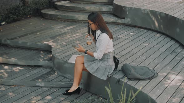 Asian Attractive Young Woman with Glasses Uses Phone on the Street