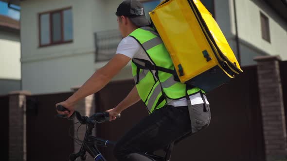 Young Man with Delivery Bag Riding Bike Looking Around Searching Client Address