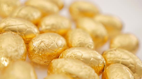 Easter chocolate eggs wrapped in golden foil grouped on white surface 4K 2160p 30fps UltraHD footage