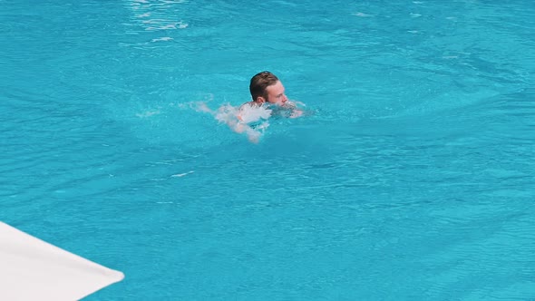 Young Guy Swims in a Swimming Pool